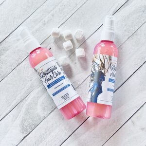 Two pink bottles of hair care spray lying next to marshmallows