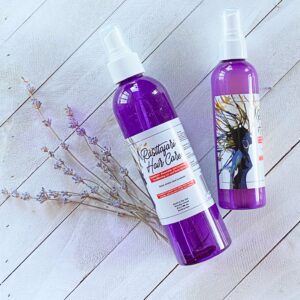 Two lavender bottles of hair care spray lying next to a lavender flower